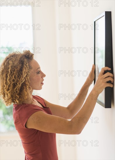 Young woman hanging print on wall.