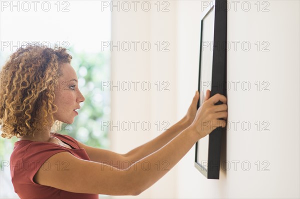 Young woman hanging print on wall.