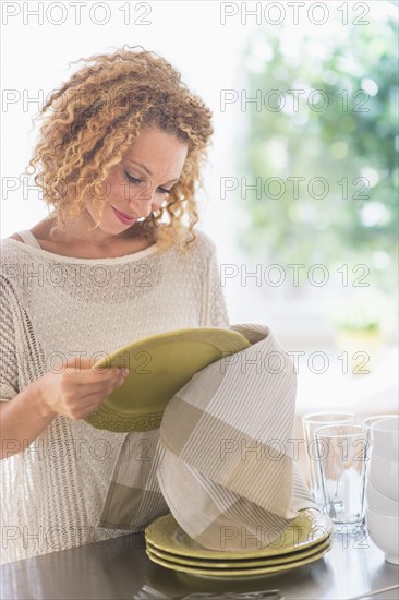 Young woman drying plates in kitchen.