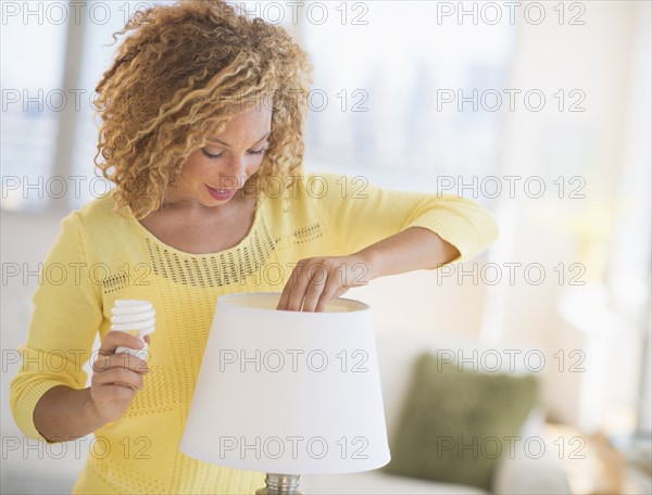 Young woman changing bulb in lamp.