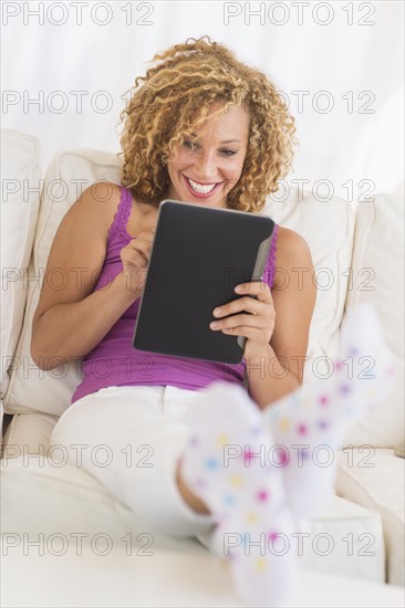 Young woman sitting on sofa with digital tablet.