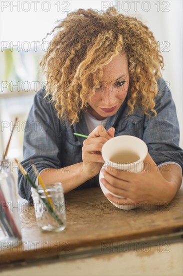 Female artist painting on ceramics in studio.