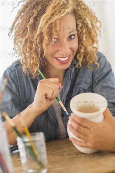 Portrait of female artist painting on ceramics in studio.