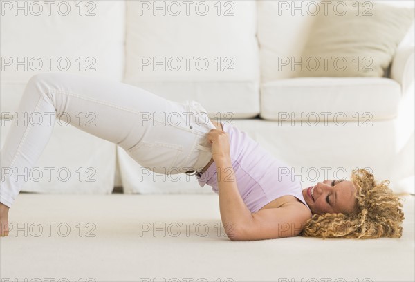 Young woman trying on tight jeans on the floor.