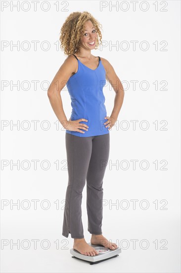 Portrait of young woman standing on weight scale, studio shot.