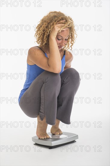 Young woman crouching on weight scale, studio shot.