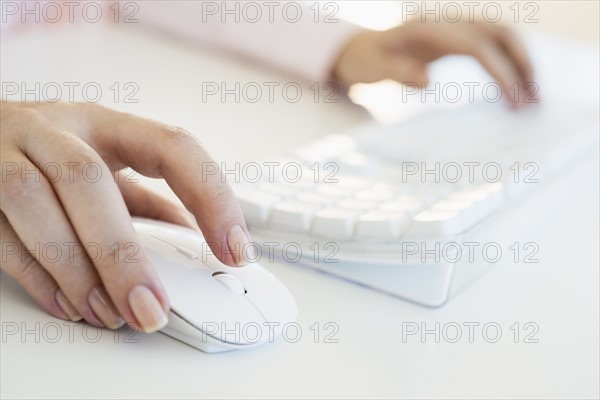 Close up of woman's hands using computer keyboard and computer mouse.