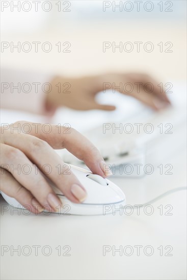 Close up of woman's hands using computer keyboard and computer mouse.