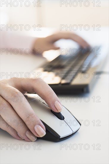 Close up of woman's hands using computer keyboard and computer mouse.