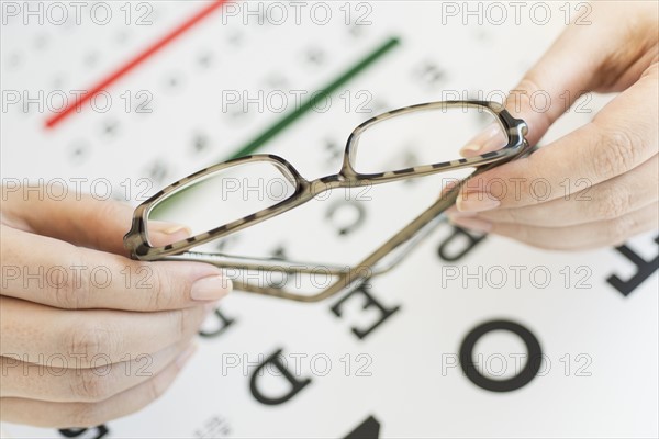 Close up of woman's hands holding glasses above eye chart, studio shot.