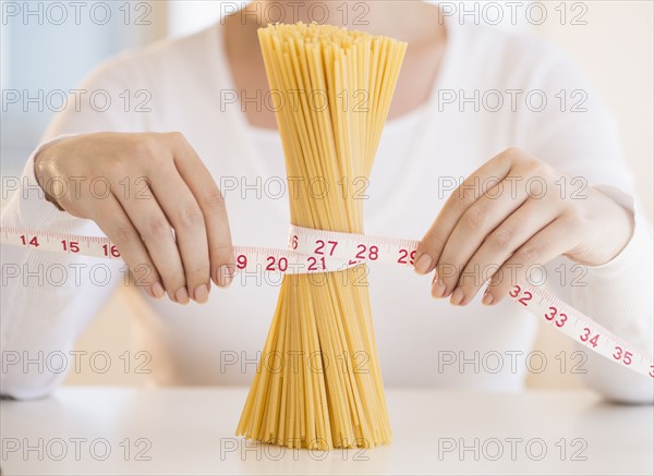 Close up of woman's hands measuring pasta with tape measure.