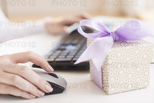 Gift box on desk next to woman using computer.