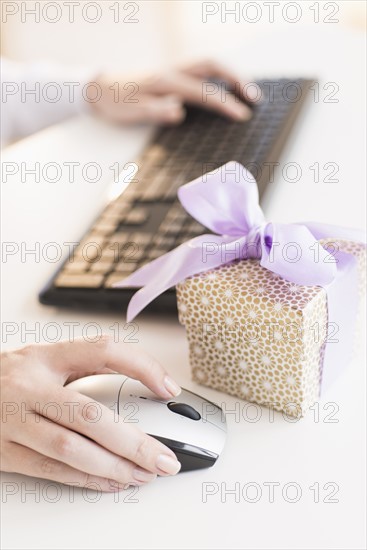 Gift box on desk next to woman using computer.