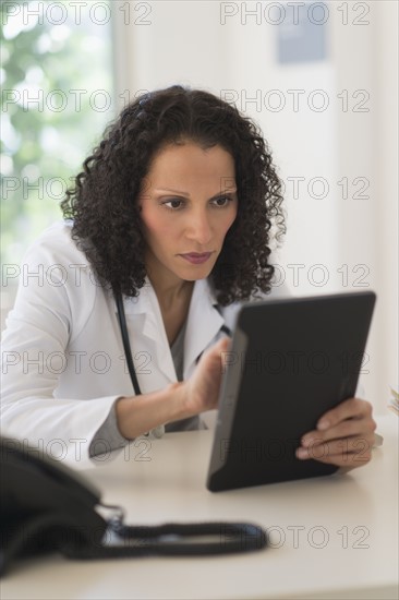 Portrait of doctor sitting in office and using digital tablet.