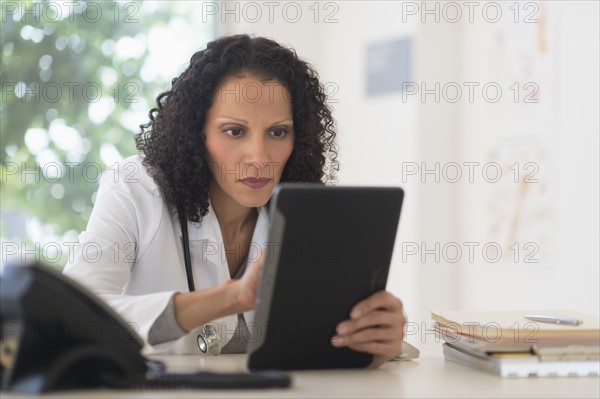 Portrait of doctor sitting in office and using digital tablet.