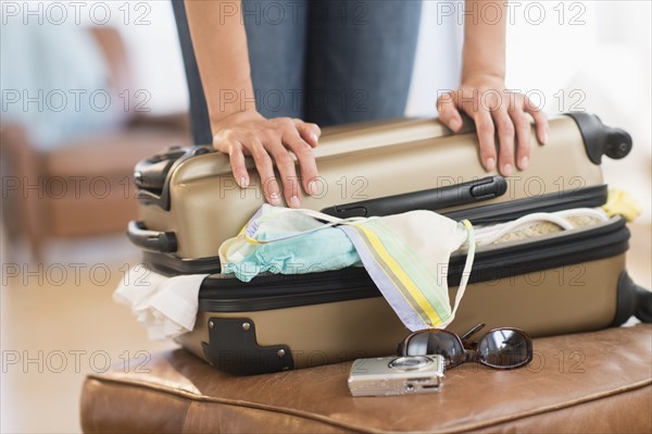 Woman trying to close full suitcase.