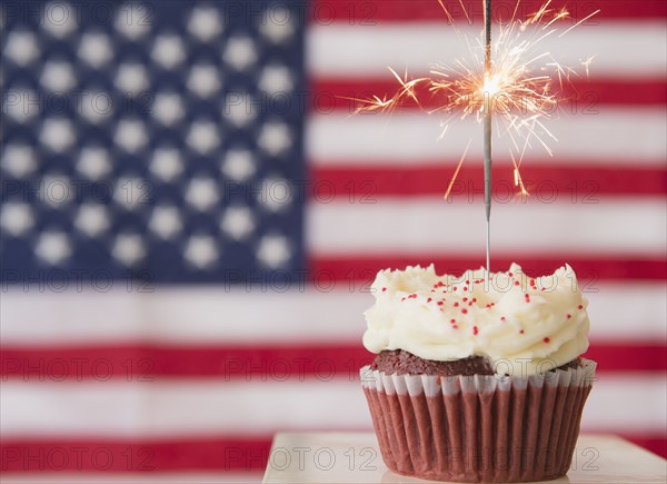 Studio shot of sparkler atop cupcake, american flag in background. Photo : Jamie Grill