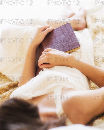 Woman in white chemise laying in bed and holding book. Photo: Daniel Grill