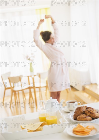 Breakfast scene with woman in white robe stretching. Photo : Daniel Grill