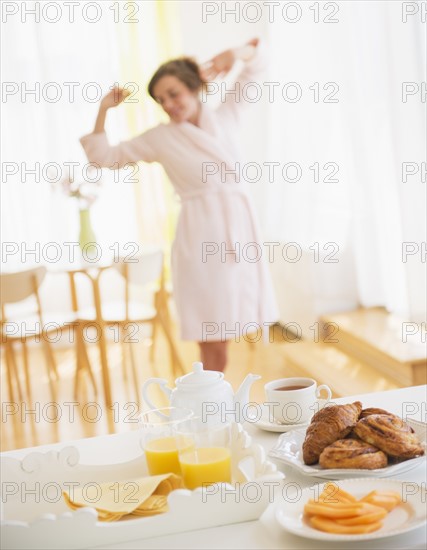 Breakfast scene with woman in white robe stretching. Photo : Daniel Grill