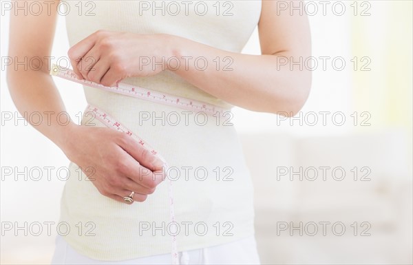 Young woman with tape measure wrapped around waist, midsection. Photo : Daniel Grill