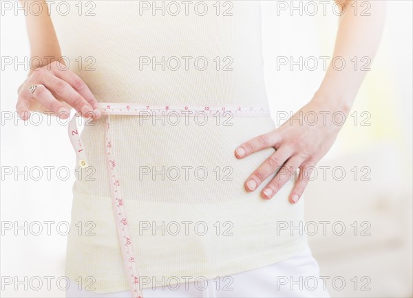 Young woman with tape measure wrapped around waist, midsection. Photo : Daniel Grill