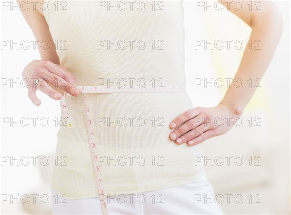 Young woman with tape measure wrapped around waist, midsection. Photo : Daniel Grill