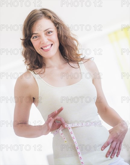 Young woman with tape measure wrapped around waist. Photo : Daniel Grill