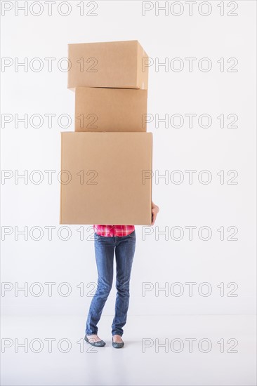 Studio shot of young woman carrying stack of boxes. Photo : Daniel Grill