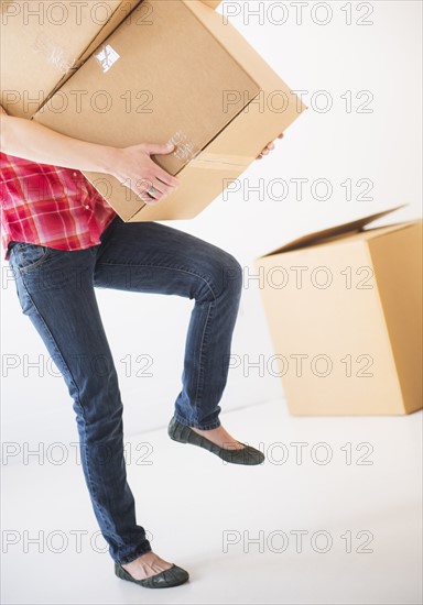 Studio shot of young woman carrying stack of boxes, low section. Photo : Daniel Grill