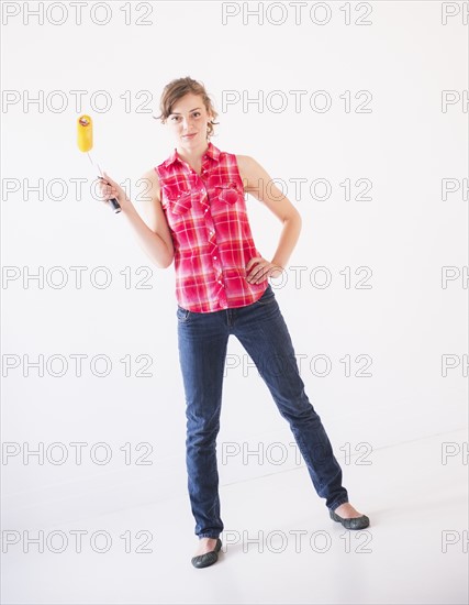 Studio shot of young woman holding paint roller. Photo: Daniel Grill