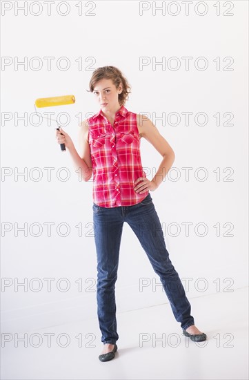 Studio shot of young woman holding paint roller. Photo : Daniel Grill