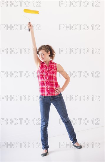 Studio shot of young woman holding paint roller. Photo : Daniel Grill