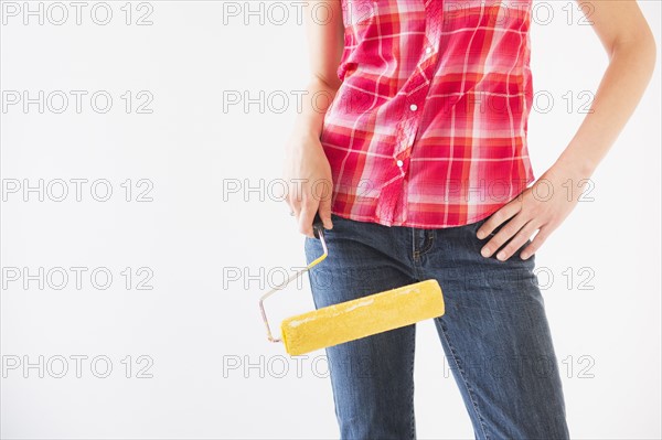 Studio shot of young woman holding paint roller, midsection. Photo : Daniel Grill