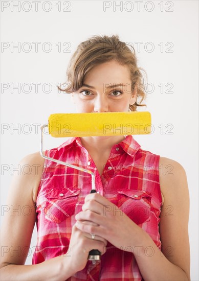 Studio shot of young woman holding paint roller. Photo: Daniel Grill