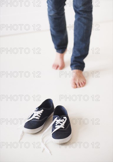 Studio shot of young barefoot woman standing next to shoes, low section. Photo : Daniel Grill