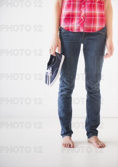 Studio shot of young barefoot woman holding shoes, low section. Photo : Daniel Grill