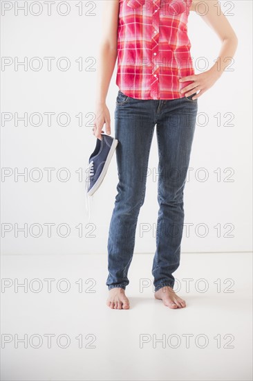 Studio shot of young barefoot woman holding shoes, low section. Photo : Daniel Grill
