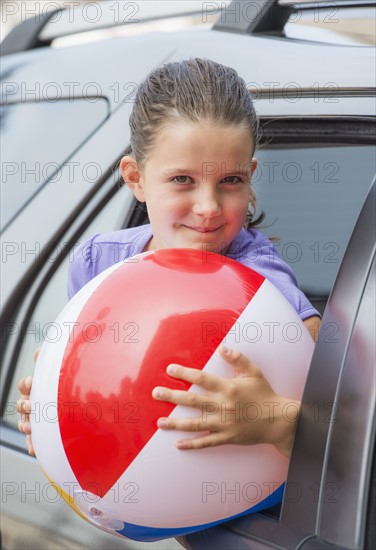 Young girl (8-9) with beach ball peeking through car window . Photo : Daniel Grill