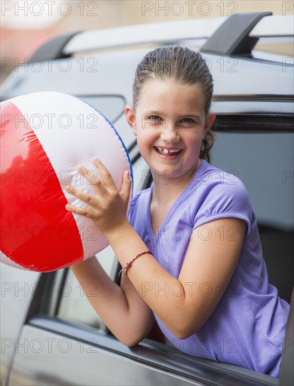 Young girl (8-9) with beach ball peeking through car window . Photo: Daniel Grill