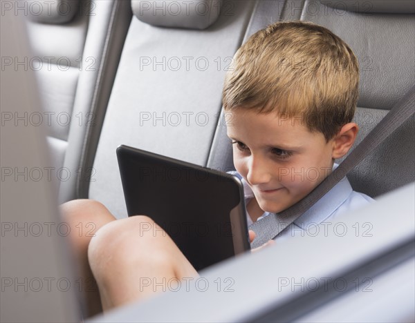 Boy (6-7) using digital tablet while sitting in car. Photo : Daniel Grill