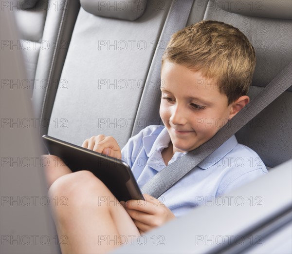 Boy (6-7) using digital tablet while sitting in car. Photo: Daniel Grill