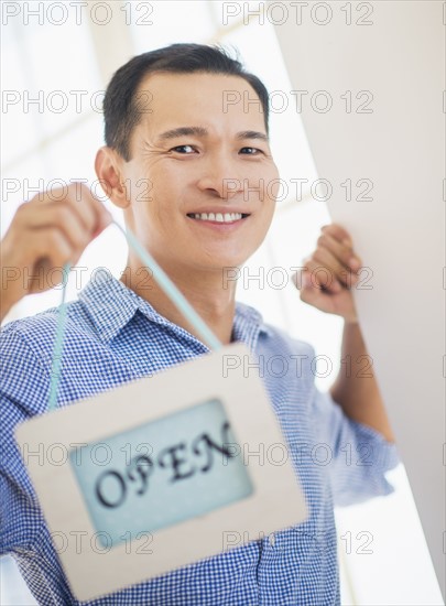 Mid adult man holding open sign. Photo : Daniel Grill