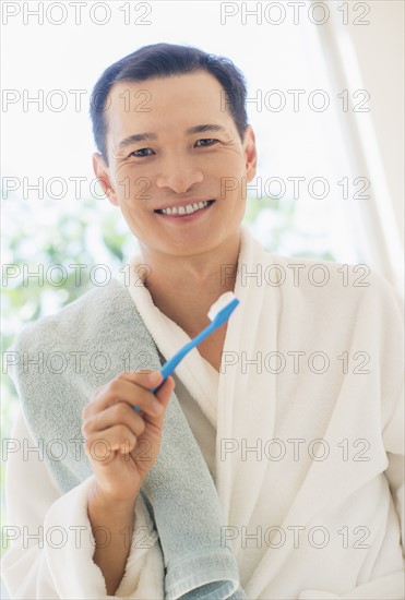 Happy mid adult man holding toothbrush. Photo : Daniel Grill