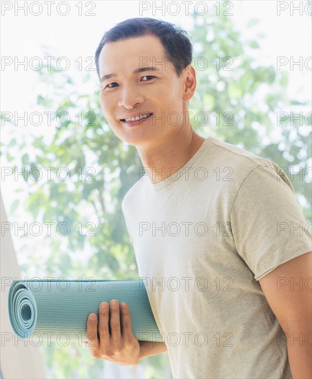 Happy mid adult man holding exercising mat. Photo : Daniel Grill