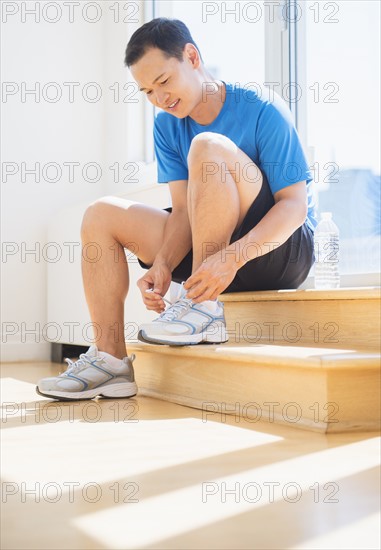 Mid adult man lacing his running shoes. Photo : Daniel Grill