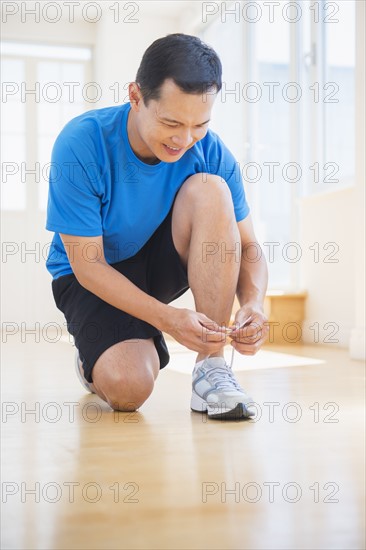 Mid adult man lacing his running shoes. Photo : Daniel Grill