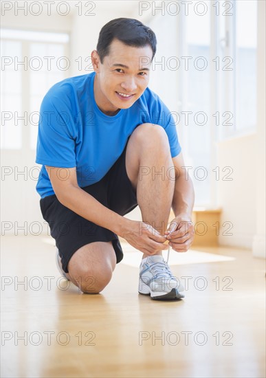 Mid adult man lacing his running shoes. Photo : Daniel Grill