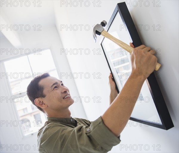 Mid adult man hanging picture on wall. Photo : Daniel Grill