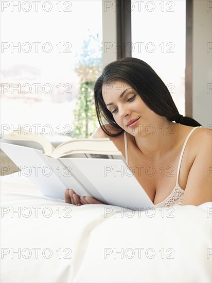 Young attractive woman reading book in bed.